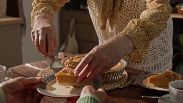 Senior woman slicing and serving homemade pumpkin pie to family member during holiday dinner. Footage is perfect for Thanksgiving promotions and family lifestyle campaigns