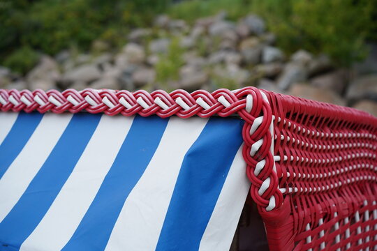 Detailansicht eines rot-wei&szlig;en Strandkorbs mit Zopfgeflecht an der Ostsee in der L&uuml;becker Bucht