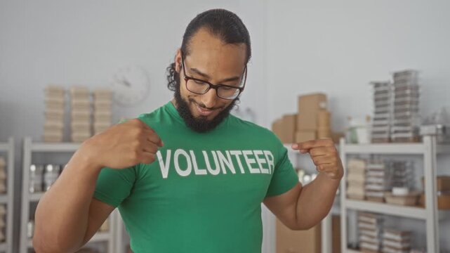 Man points finger to volunteer shirt and smiles with folded arms among packed shelves in a donation center building; community service pride.