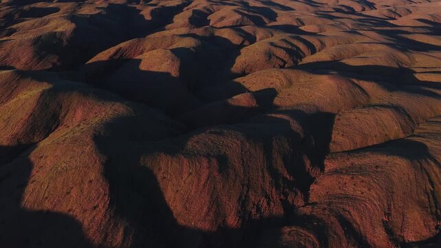 Aerial view shows rounded granite domes and eroded ridges near Spitzkoppe, Namibia. A slow sweep reveals narrow gullies and warm golden hour light with deep shadows.
