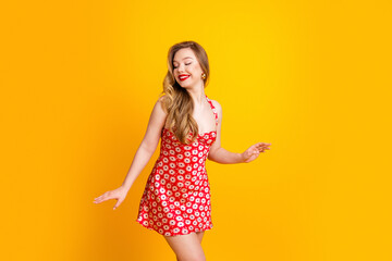Smiling woman in red daisy dress dancing against a bright yellow background, summer fashion...