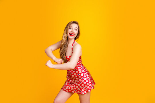 Happy young woman in a red floral summer dress dancing joyfully against a bright yellow background, retro style portrait showing energy, confidence and playful summer fashion
