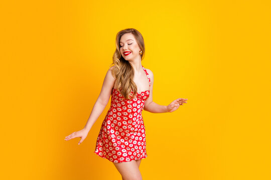 Smiling woman in red daisy dress dancing against a bright yellow background, summer fashion portrait conveying joy and retro style