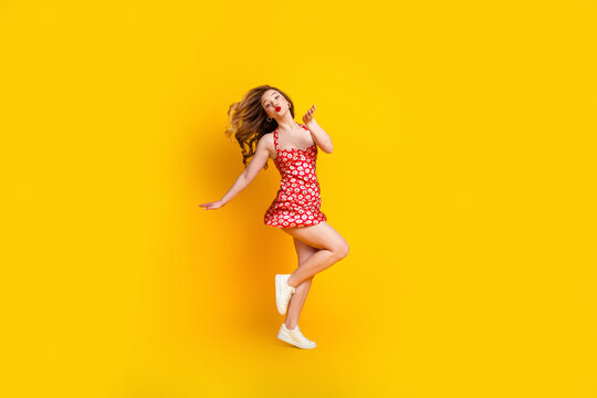 Young woman in red floral dress jumping joyfully against a bright yellow background, summer fashion, playful energy and carefree style