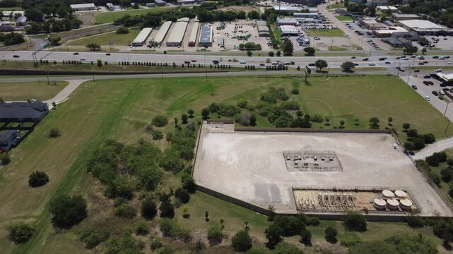 Energy production facility borders retail centers along Wilshire Blvd in suburbs of Fort Worth. Elevated perspective highlights gas infrastructure near commercial zones in Burleson, TX
