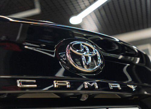 Shiny chrome Toyota corporate logo emblem badge and Camry XV70 model name lettering on glossy black trunk lid panel surface of modern Japanese executive sedan car clean luxury vehicle details close-up