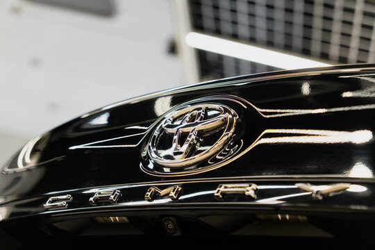 Shiny chrome Toyota corporate logo emblem badge and Camry XV70 model name lettering on glossy black trunk lid panel surface of modern Japanese executive sedan car clean luxury vehicle details close-up