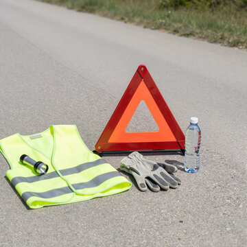 road safety kit with warning triangle, reflective vest, gloves on rural road, concept of safe driving