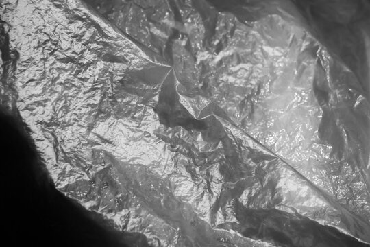 Crinkled plastic sheet reflective texture abstract lighting glossy surface subtle contrast dramatic mood