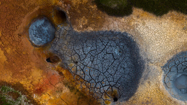 Aerial view of geothermal mud pools with cracked, colorful earth and bubbling volcanic terrain in Husavik, Nordurthing, Iceland.