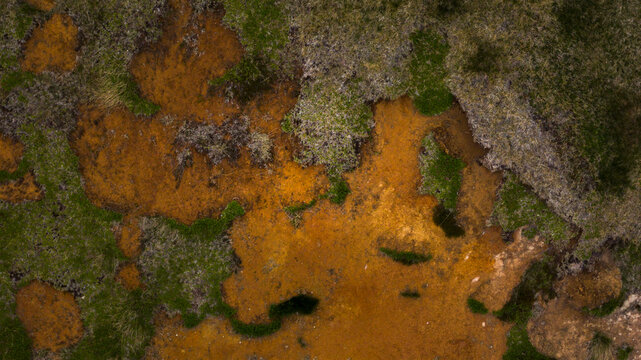 Aerial view of geothermal ground patterns with vibrant orange mineral deposits and patches of green moss in the Icelandic landscape Husavik, Nordurthing, Iceland.
