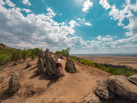 Wide angle shot of the granite monoliths known as Dinosaur Eggs rock formations overlooking arid hills under a cloudy blue sky in Macin Mountains, Dobrogea, Romania.