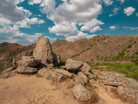 Wide angle shot of the granite monoliths known as Dinosaur Eggs rock formations overlooking arid hills under a cloudy blue sky in Macin Mountains, Dobrogea, Romania.
