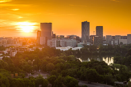 Panoramic sunset view over modern business district skyline and lush green park in Bucharest Romania during warm golden hour