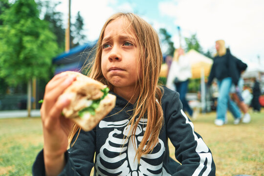 Girl in a skeleton hoodie holding a chicken sandwich at a festival