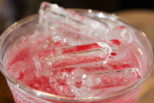 Pink fruit drink with clear ice cubes glistening in plastic cup, refreshing cold beverage with condensation and bright color