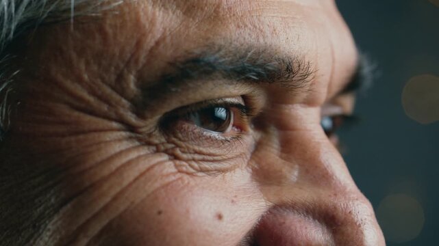 Reacting to soft key light, senior man's right eye squinting and blinking in close-up with glint
