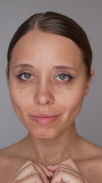 Close-up portrait of young woman touching cheek, showing refined facial contour and slimmer lower face after buccal fat pad removal on gray background