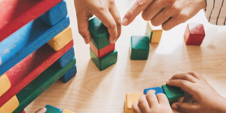 Early childhood education and brain development in children along with learning with kids who are stacking colorful wooden blocks while adults guide them