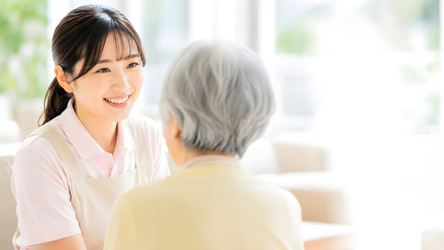 視線をしっかり合わせながら高齢の女性に優しく語りかける笑顔の女性介護スタッフ