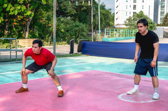 Two male sepak takraw players standing in defensive stance, concentrating intensely to receive and defend an incoming serve from the opposing team during a match on outdoor court
