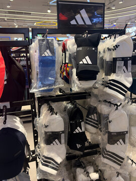 Athletic caps and accessories are displayed on a retail rack. The products feature the Adidas logo prominently, showcasing a variety of styles and colors. The setting is a well-lit store.
