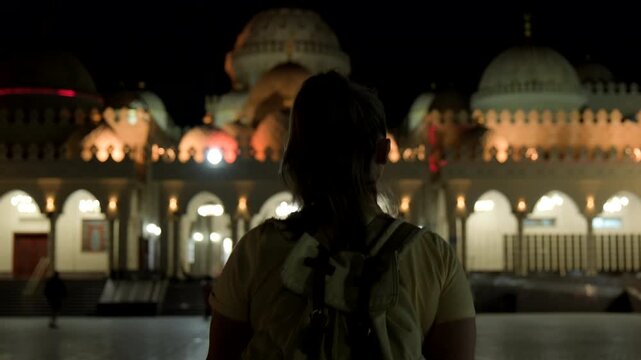 Woman tourist walking towards illuminated Al Mina Mosque in Hurghada in evening