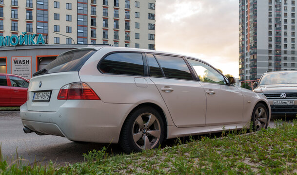 Side view of a white BMW 5-Series E61 estate car parked on a city street. German luxury station wagon automobile near a modern colorful residential building facade. Urban transportation. 