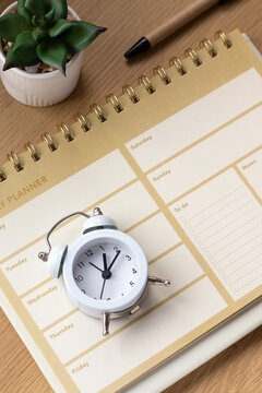Alarm clock and weekly planner notebook on a wooden desk. The concept of goals, time management, and productivity.