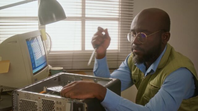African American man repairing retro desktop computer with screwdriver, pausing in frustration to rub forehead. Footage is perfect for IT support and hardware troubleshooting ads