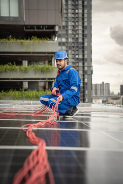 Solar Technician Routes and Organizes Electrical Cables Across Rooftop Photovoltaic Panels During Renewable Energy System Installation on an Urban Building
