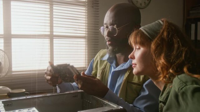 African American man explaining computer hardware to young adult Caucasian woman and installing graphics card into PC tower. Perfect for IT support and tech education marketing