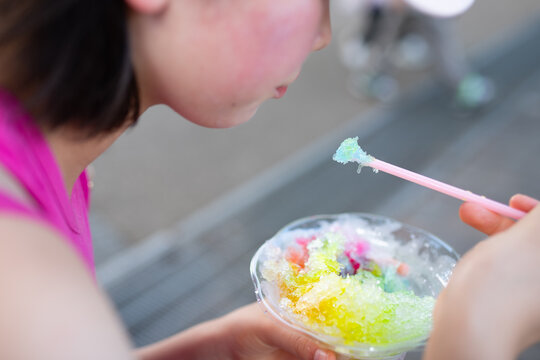 夏の屋外でカラフルなレインボーかき氷を食べる女の子