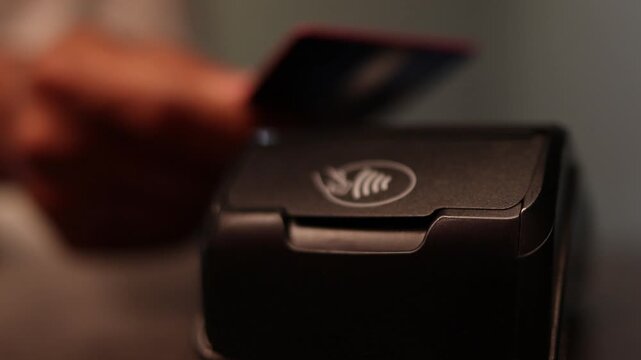 Customer swiping a credit card on a terminal reader for contactless payment at a counter with blurry background