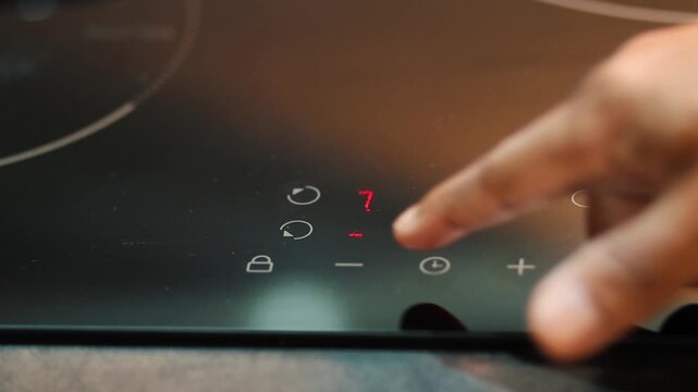 Person adjusting digital timer and temperature on modern induction cooktop with touch controls