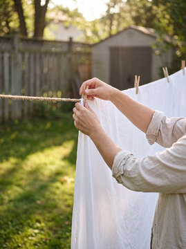 Woman hanging clean white laundry on outdoor clothesline in sunlit yard