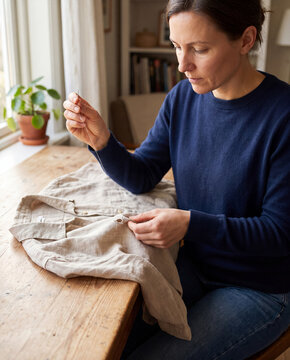 Woman mending a torn linen shirt with needle and thread at wooden table