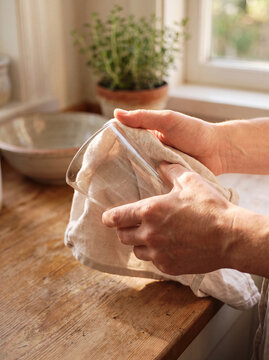 Close up of hands drying clean glass tumbler with soft cotton kitchen towel