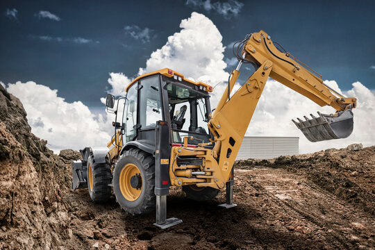 Excavator loader performs work on a construction site moving soil and rocks during daylight hours with clouds in the blue sky