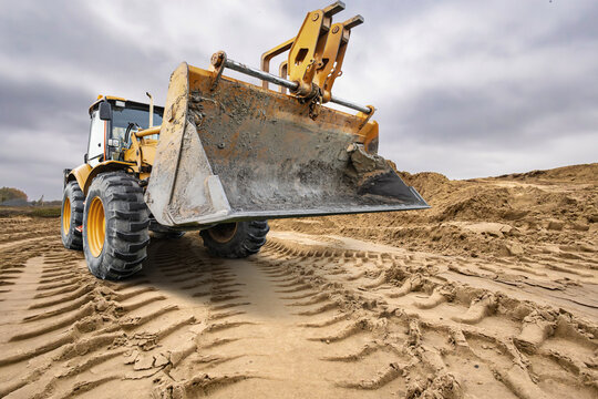 A universal excavator loader is at a construction site during daylight hours. It is moving dirt and leveling the ground. The area shows recent work on the terrain