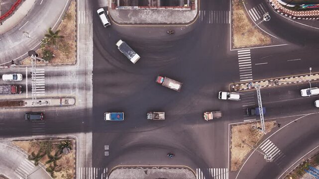 Drone aerial view of a busy city intersection featuring an underpass, multiple traffic lanes, cars, motorcycles, pedestrian crossings, and urban road infrastructure. The image represents transportatio