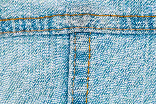 Closeup view of blue denim fabric with orange stitching detail. Textured jeans material background. Textile industry concept, garment manufacturing design and fashion clothing accessory