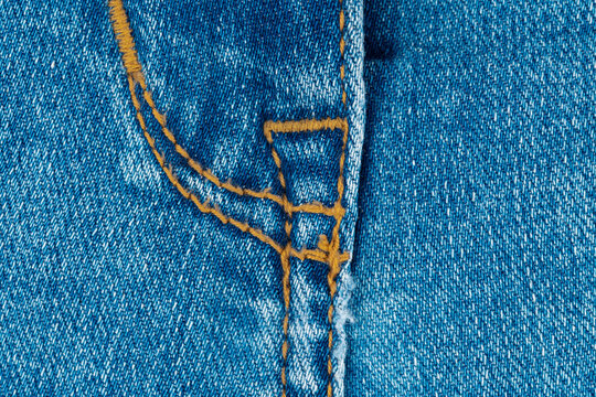 Blue denim jeans texture with close up fly stitch detail. Fabric pattern of cotton material for fashion clothing industry. Textile background with orange thread seam for apparel