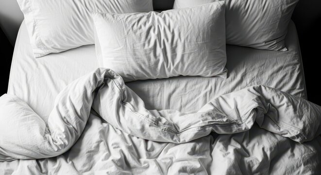 Top View of a Messy Unmade Bed with White Sheets Pillows and Duvet in High Contrast Light