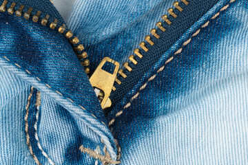 Macro detail of blue denim jeans with open brass zipper and stitching © Alexander Piragis