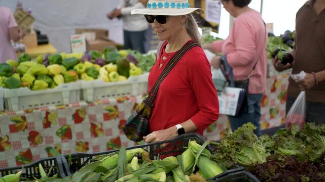 Happy woman shops for fresh produce at the farmers market in Sonoma, California, on a sunny morning. She picks fruits and vegetables.