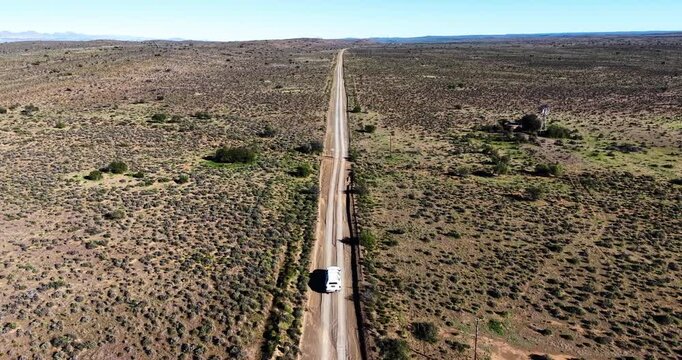 Aerial of a 4x4 vehicle travelling along a remote gravel road. A traditional farm windmill and water reservoir stand beside the road, capturing the timeless beauty of the South African Karoo.