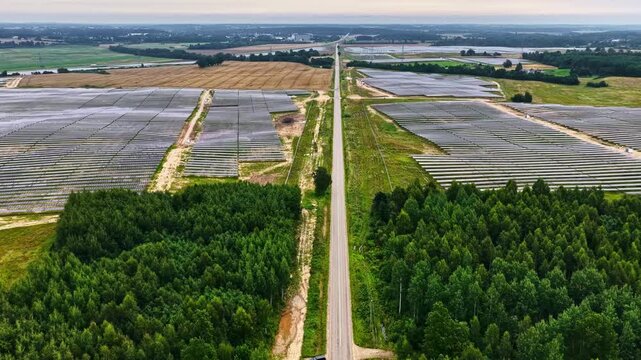 Aerial view of a large solar farm divided by a straight road, surrounded by forests and fields in Tume, Tukums Municipality, Latvia.