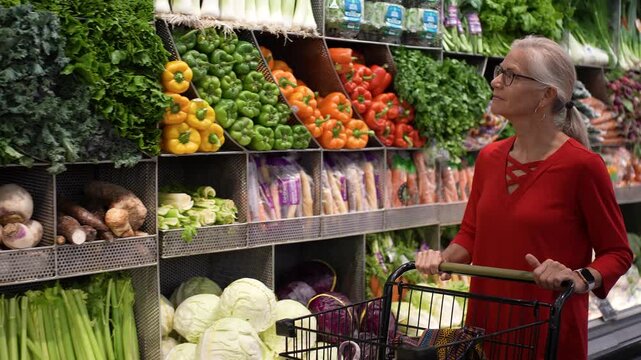 A woman picks fresh fruits and vegetables at a grocery store while smiling and looking happy.