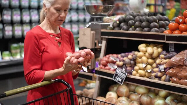 A senior woman smiles as she shops for fresh fruits and vegetables in a grocery store, carefully choosing her produce.